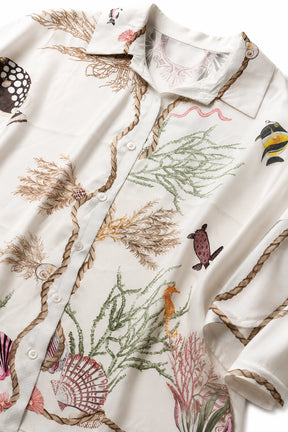 An off-white long-sleeve button-up shirt featuring a detailed undersea-themed print with seashells, coral, rope borders, and small sea creatures.
