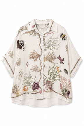 An off-white short-sleeve button-up shirt featuring a detailed underwater-themed print with seashells, coral, seaweed, and small fish, finished with gold-toned rope trim along the edges.