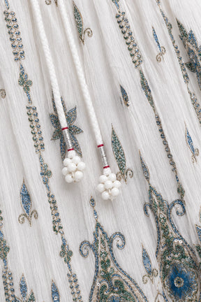 Close-up of a white embroidered fabric with blue and green paisley patterns and white beaded drawstring tassels.