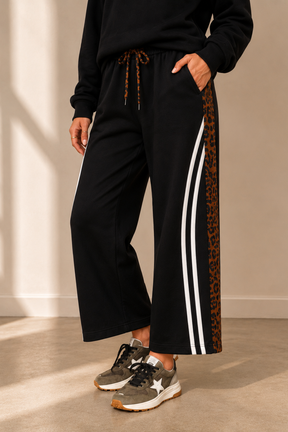 Person wearing black pants with leopard print and white stripes, standing against a neutral background.