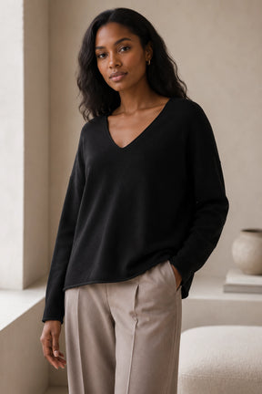 Woman wearing a black sweater and beige pants in a neutral setting