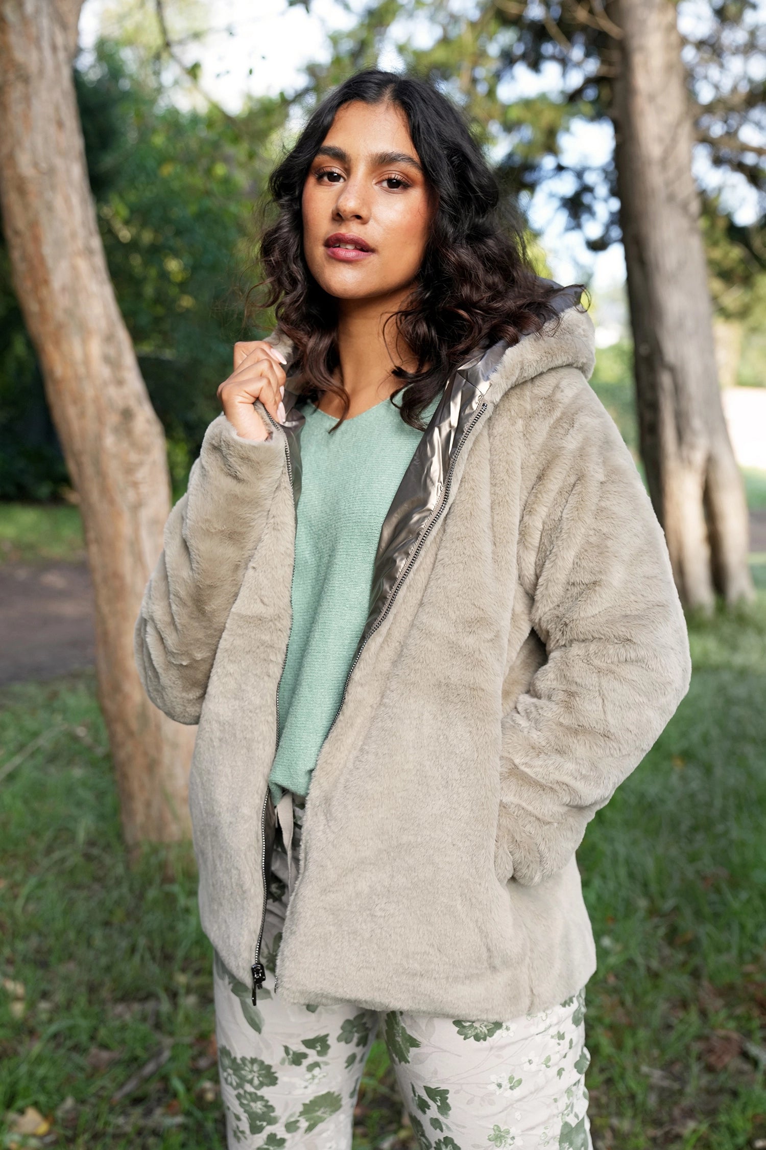 Woman wearing a beige jacket outdoors with trees in the background