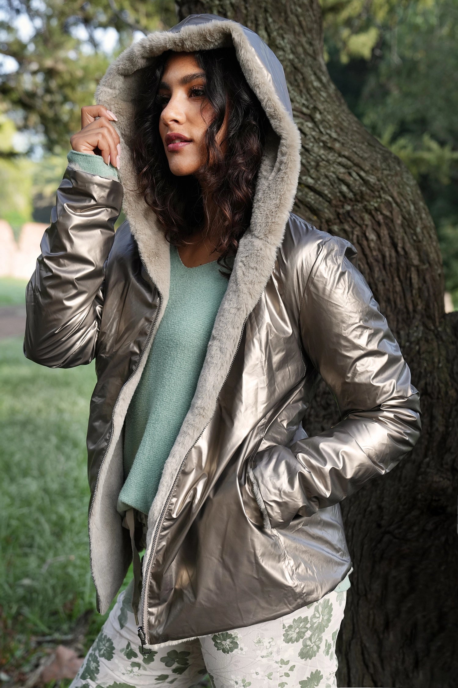 Woman wearing a silver puffer jacket with a hood in an outdoor setting.