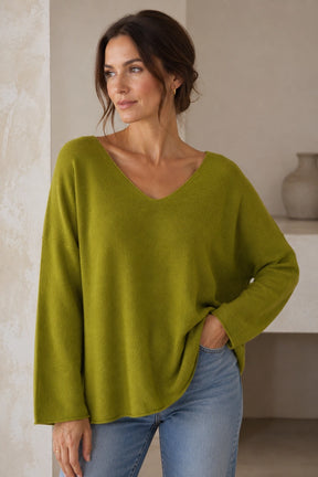 Woman wearing a green sweater and blue jeans indoors.