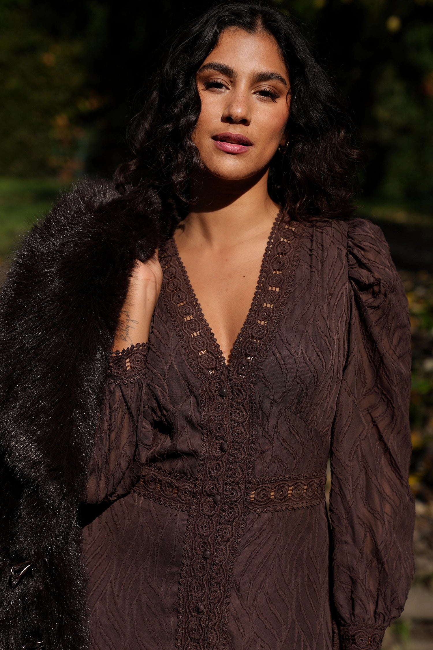 Woman wearing a dark brown lace dress with a fur coat in a forest setting