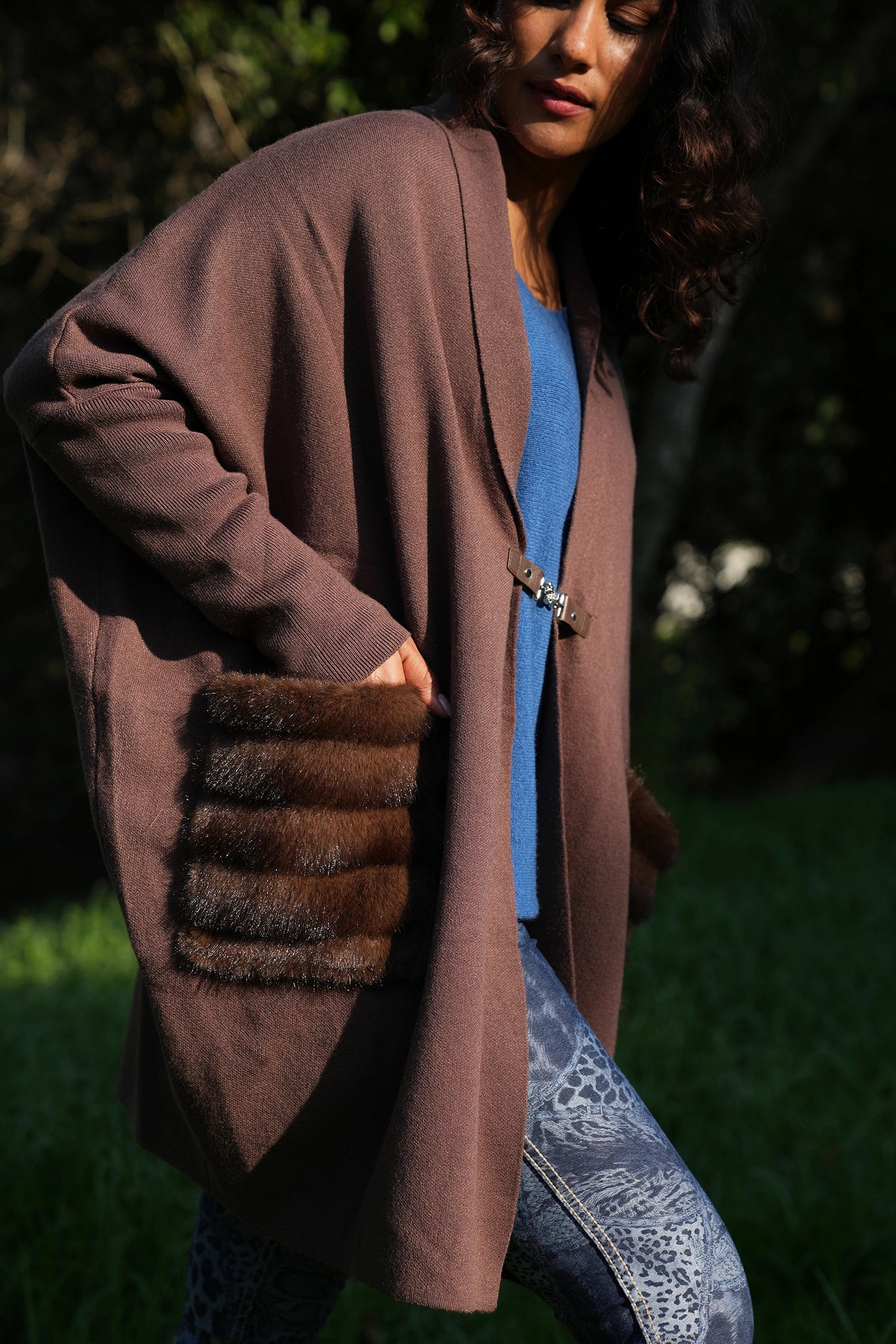 Person wearing a long brown coat with fur-trimmed pockets outdoors.