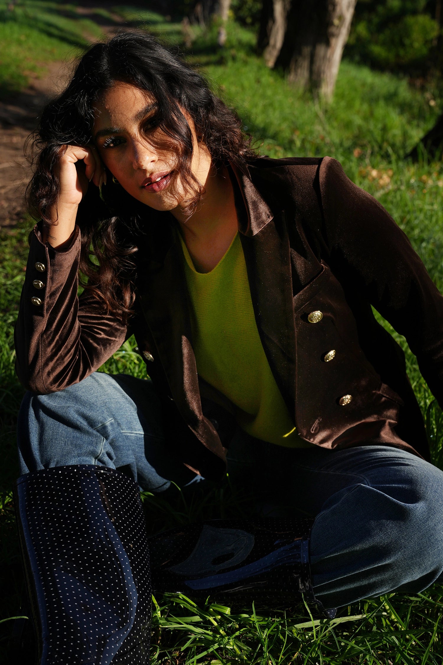 Person sitting on grass wearing a brown jacket and blue jeans.