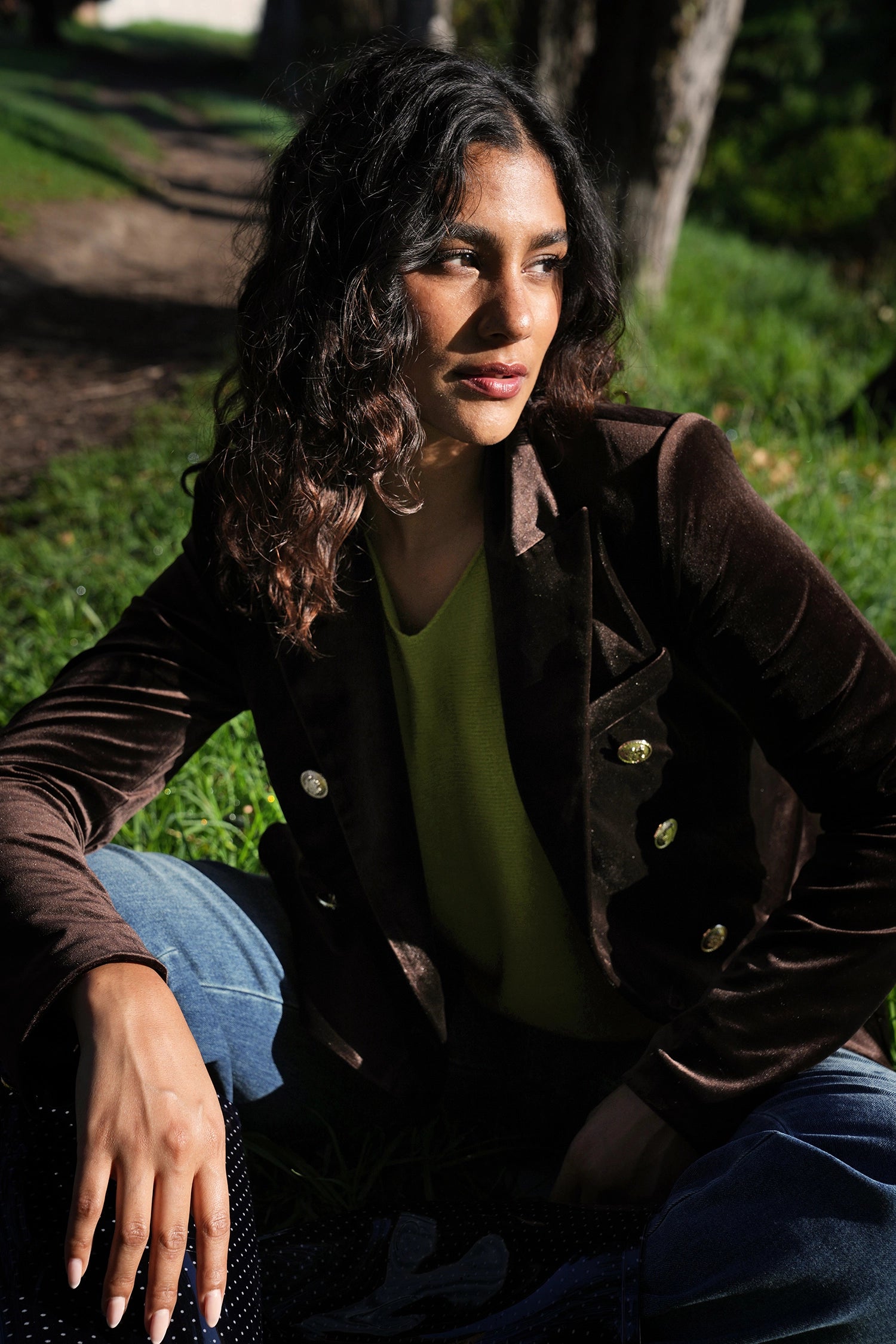 Woman sitting outdoors on grass wearing a brown jacket and green shirt