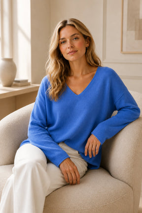 Woman wearing a blue sweater sitting on a beige armchair in a well-lit room.