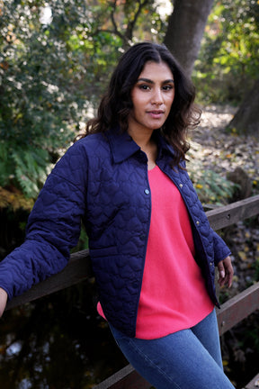 Woman wearing a navy quilted jacket over a pink shirt in an outdoor setting