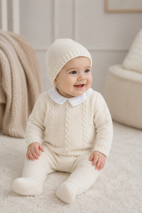 Baby wearing a cream knit outfit sitting on a soft surface