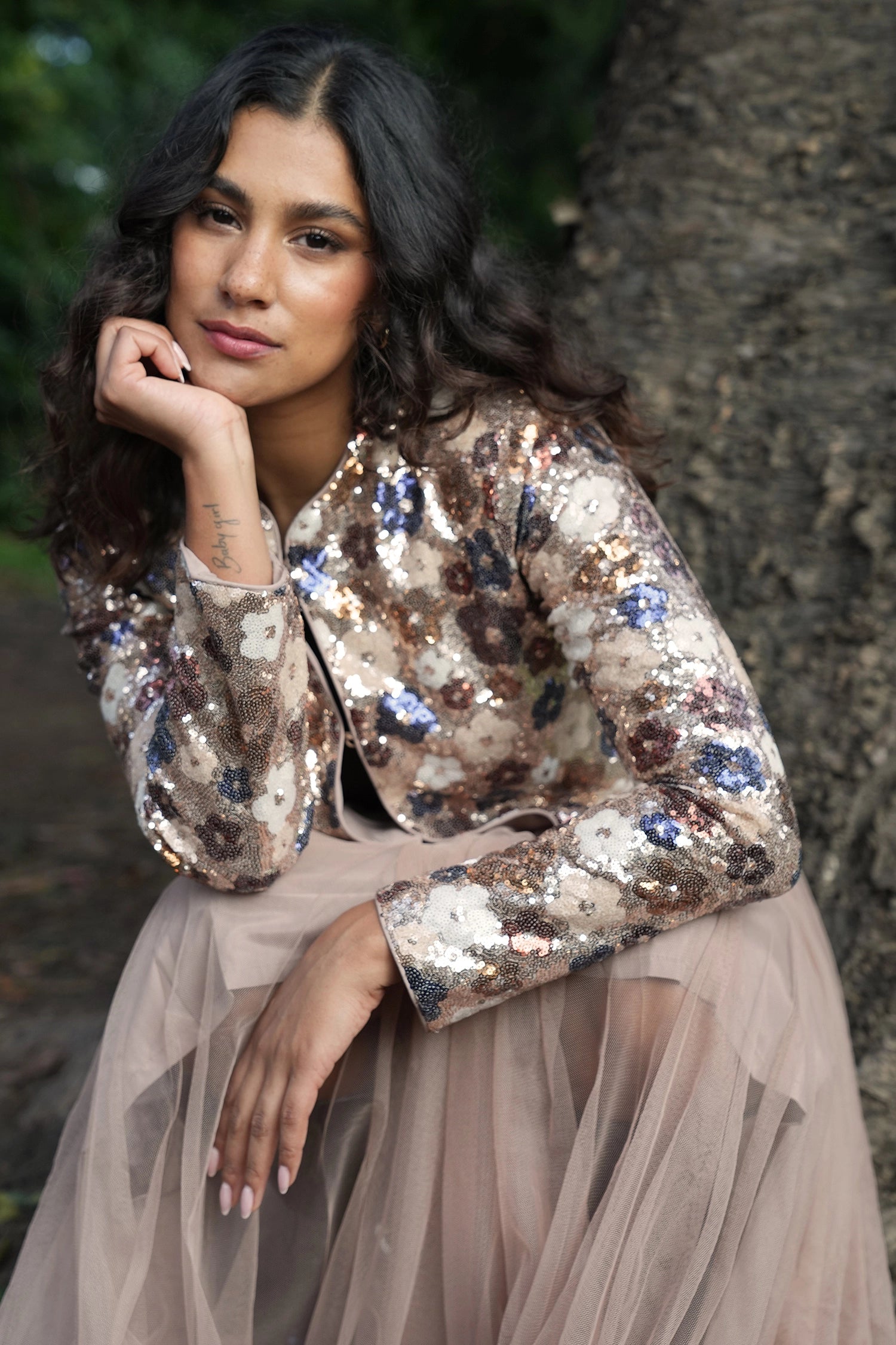 Woman wearing a sequined jacket and beige dress against a natural background