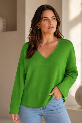Woman wearing a green sweater and blue jeans indoors