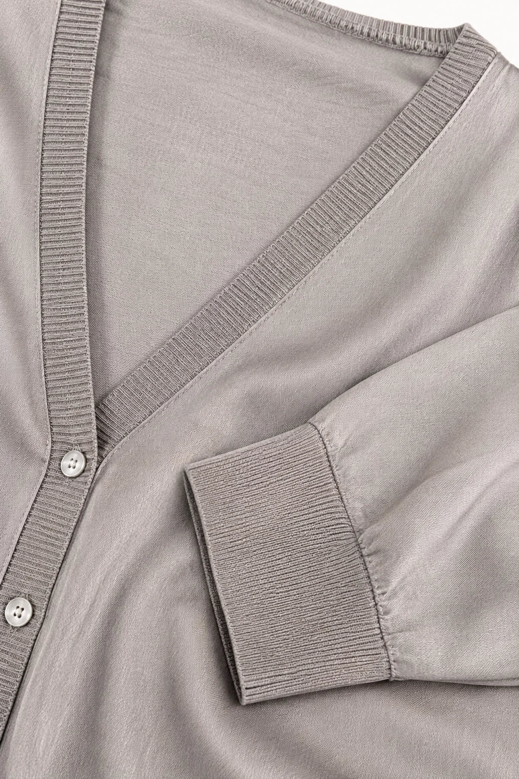 Close-up of a light taupe knit cardigan featuring a V-neckline, ribbed trim, and a buttoned placket.