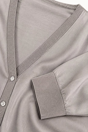 Close-up of a light taupe knit cardigan featuring a V-neckline, ribbed trim, and a buttoned placket.