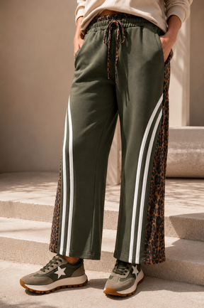Person wearing green jogger pants with white stripes and leopard print details, standing on steps.