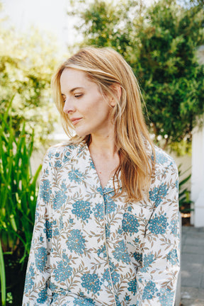Woman wearing a floral patterned shirt outdoors with greenery in the background