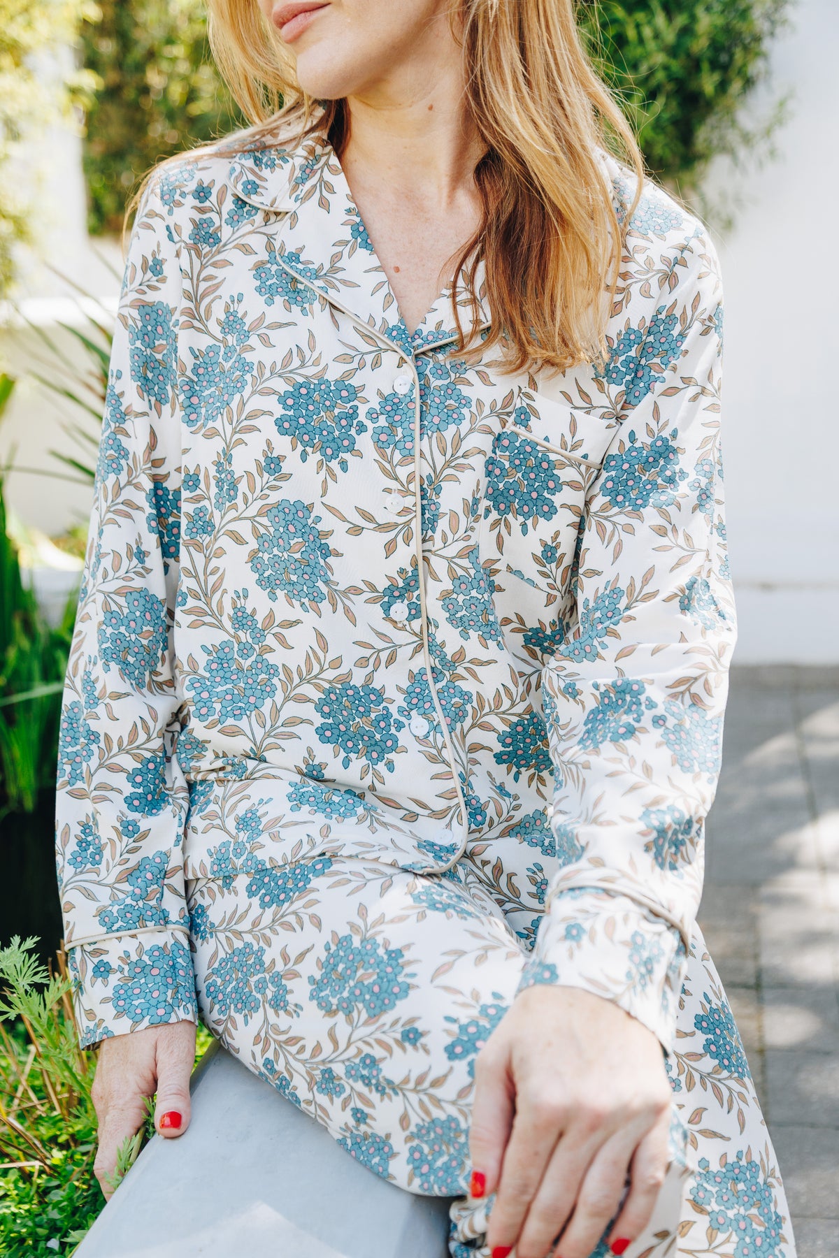 Woman wearing a floral long-sleeve shirt sitting outdoors.