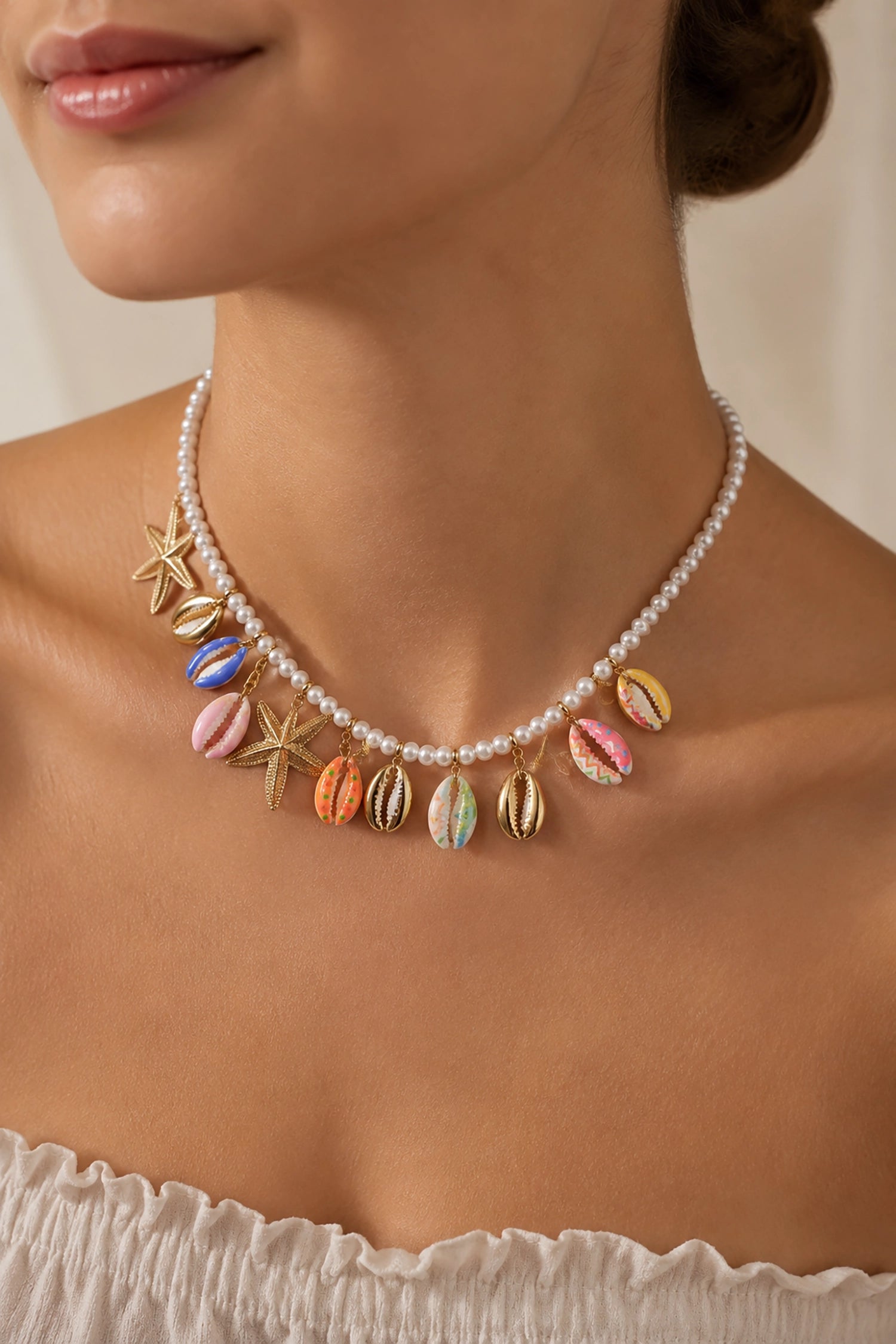 Necklace with colorful shell-like pendants and starfish charms on a person wearing a white top.