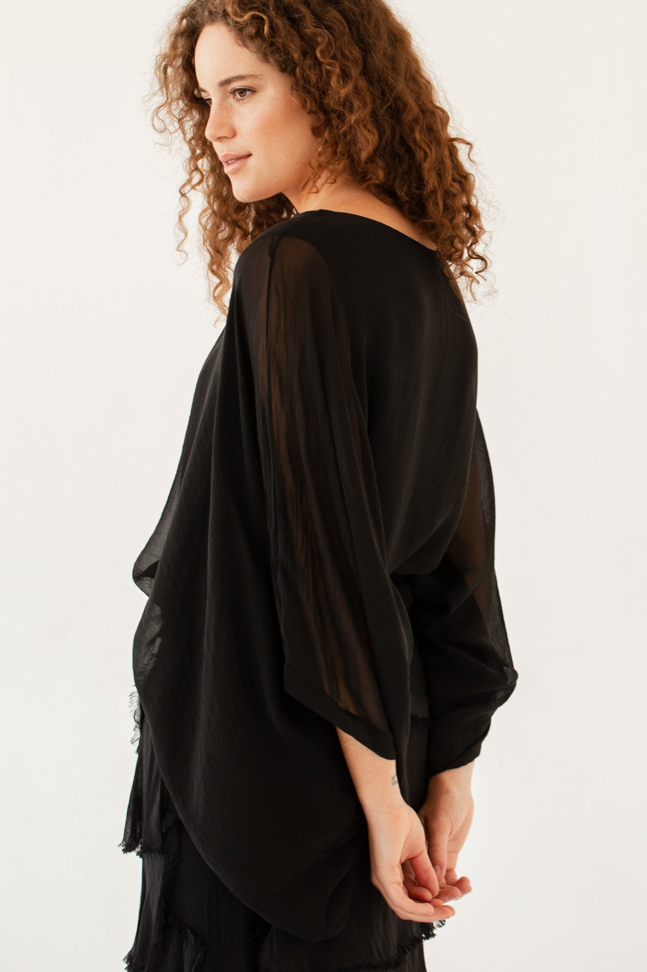 Back view of black silk poncho top with flowing sheer sleeves on model