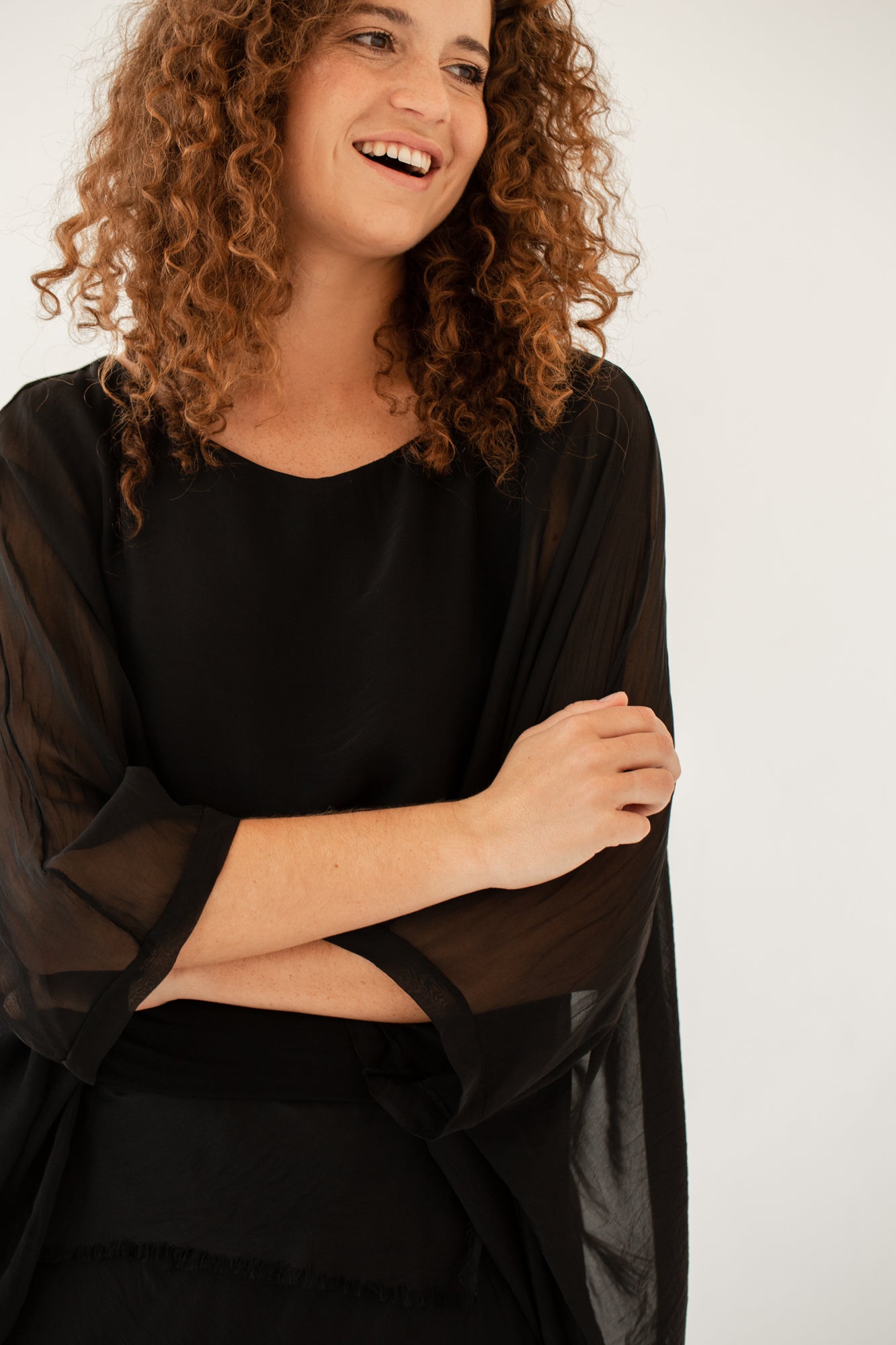 A woman wearing a green silk poncho with a classic boat neckline and long, dropped sleeves.